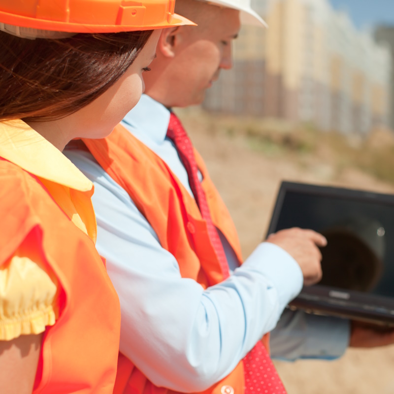Two architects wearing protective helmet works in front of building site